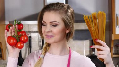 Komik kadın elinde uzun makarna ve taze domatesle spagetti pişirmeyi düşünüyor..