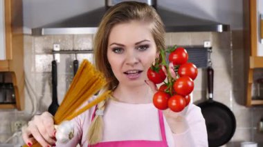 Komik kadın elinde uzun makarna ve taze domatesle spagetti pişirmeyi düşünüyor..