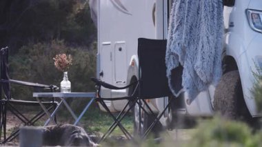 Köpek karavanın yanında yatıyor. İnsanların doğanın tadını çıkarması için masalı ve sandalyeli bir karavan. Doğada kamp yapmak. Karavan tatili. Evcil hayvanla seyahat etmek.