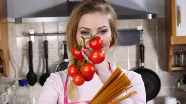 Komik kadın elinde uzun makarna ve taze domatesle spagetti pişirmeyi düşünüyor..