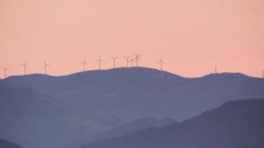 Akşam manzarası. Gün batımında tepede rüzgâr türbinleri çiftliği.