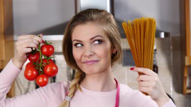 Komik kadın elinde uzun makarna ve taze domatesle spagetti pişirmeyi düşünüyor..