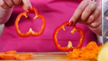 Salata yapan kişi. Kadın eli kesme tahtasında iki parça kırmızı dolma biber halkası gösteriyor..