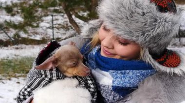 Köpeğiyle oynayan genç bir kadın, pinscher ratter prazsky krysarik, kış havasında dışarıda. Dişi köpek yavrusuna sevgiyle sarılıyor..