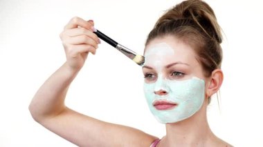 Yüzüne yeşil çamur maskesi dayayan genç bir kadın. Genç kız yağlı cildiyle ilgileniyor, gözenekleri temizliyor. Güzellik tedavisi. Cilt bakımı.