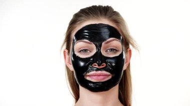 Yüzünde karbonhidratlı siyah kabuk soyma maskesi olan genç bir kadın. Kozmetik, beyazın üzerinde çıkarmaya hazır. Yağlı ciltle ilgilenen genç bir kız. Güzellik tedavisi. Cilt bakımı.