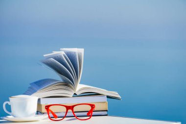 Tatilde okumak. Kahve fincanı, kitap ve kırmızı bardaklar mavi deniz suyuna karşı. Tatil gezisinde dinlenmek. Zihinsel sağlık sorunları.