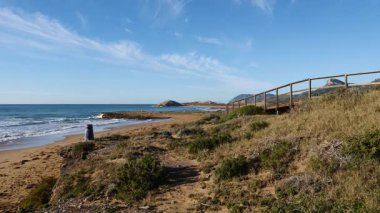 Sahil manzarası, deniz suyuna giden ahşap yolu olan kayalık deniz kıyısı. Cala Magre Sahili, Calique Bölgesel Parkı, Murcia Bölgesi İspanya.