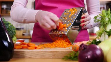 Kadının el rendeleyici havucu mutfak tahtasında yavaş çekimde sebze rendesi kullanarak yakın çekim..