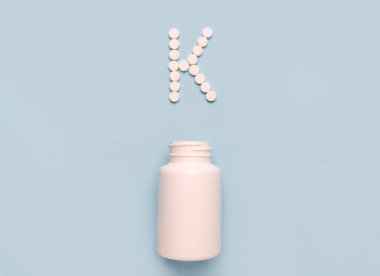 Tabletlerdeki K vitamini fillokinon ikonu ve mavi arka plandaki ilaç şişesi. Vitamin ve minerallerin çarpışması 