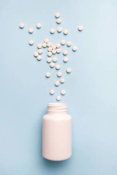 Medicaments pills spilled from a white bottle. Healthy and medicine concept on blue background
