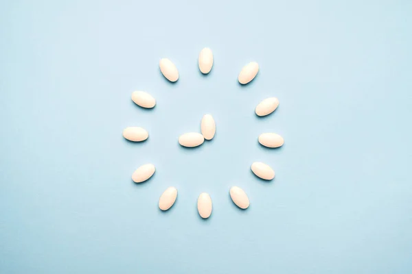 Time to take pills. Clock created from white pills on  blue background. Right time for using medicines