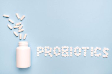 Cesaret koruması. Haplardan yapılmış probiyotik kelime, beyaz bir şişeden dökülen ilaçlar. Mavi arkaplanda. 