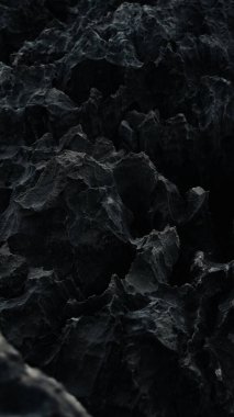 Keskin, pürüzlü karanlık kaya oluşumları dramatik ve desenli bir manzara yaratır. Yüzey pürüzlü ve gölgeli, gizemli ve doğal bir hava veriyor.