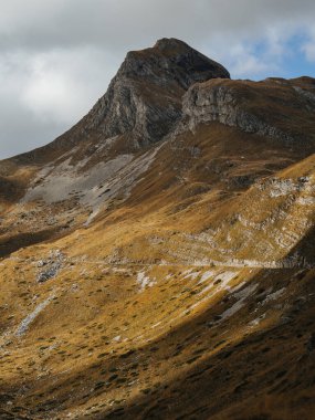 Güneş ışığıyla aydınlatılan bir dağ zirvesi. Kara bulutlar, güçlü bir ışık ve gölge zıtlığı, dramatik dağ manzarası..
