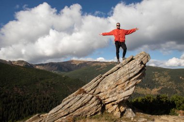 Genç bir adam bir dağın tepesinde duruyor.