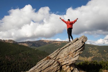Genç bir adam bir dağın tepesinde duruyor.