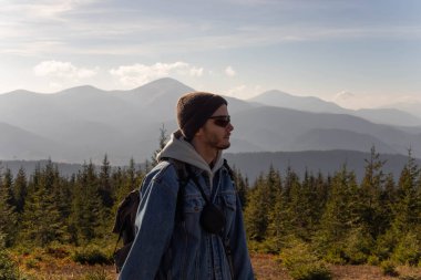 Genç bir adam bir dağ sırasının arka planında duruyor.