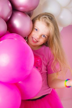 Mutlu küçük sarışın kız pembe bir arka planda balonlarla