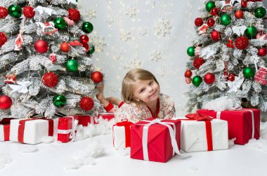 Mutlu küçük kız süslemeli Noel ağaçlarının yanındaki hediye kutularının yanında dinleniyor. Kırmızı, yeşil ve beyaz süslemeli ağaçlarla süslenmiş büyülü bir çocukluk Noel 'i..