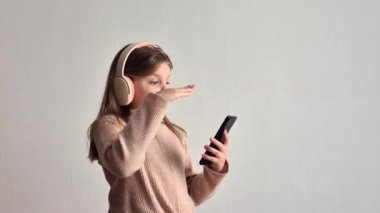 Kulaklıklı küçük kız elinde tuttuğu akıllı telefonuyla müzik dinliyor ve şarkı söylüyor.