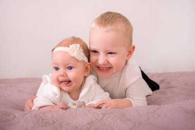 Neşeli oğlan ve küçük kız pembe arka planda yatıyorlar.