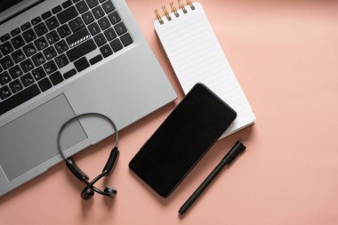 İş yeri - akıllı telefon, not defteri, dizüstü bilgisayar, kulaklık, bej arka planda kalem. Metin için boşluk olan üst görünüm