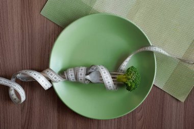 Çatalında brokoli olan yeşil tabak ve masa arkasında beyaz bir mezura. Diyet konsepti. Sağlıklı beslenme, yaşam tarzı.