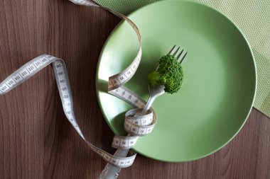 Çatalında brokoli olan yeşil tabak ve masa arkasında beyaz bir mezura. Diyet konsepti. Sağlıklı beslenme, yaşam tarzı.