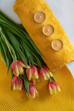 Spa konsepti. Turuncu halı üzerinde mum ve bir buket lale olan turuncu bir havlu. Sağlık ve kendine bakım kavramı.