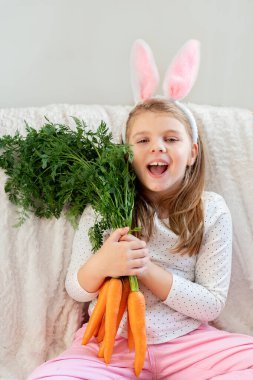 Paskalya tavşanı kulaklı, elinde taze havuçlarla gülümseyen küçük bir kız. Mutlu Paskalyalar.