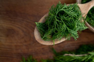 Kahverengi mutfak arka planında tahta bir kaşıkta doğranmış taze dereotu yakından çek. Donmaya hazırlanıyorum. Yemek pişirmek için aromatik bitkiler kavramı.
