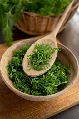 Tahta kaşıkla doğranmış dereotlu taze dereotu. Yemek pişirmek için aromatik bitkiler kavramı.