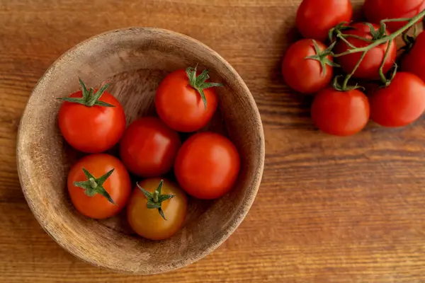 Tahta bir zeminde ahşap bir tabakta taze toplanmış kiraz domatesleri. Sağlıklı beslenme, diyet, vejetaryenlik. Yemek pişirmek. Üst görünüm.