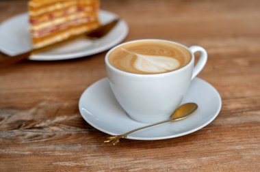 Bir fincan kahve, kafedeki ahşap bir masada bir parça kek ile kapuçino.. 