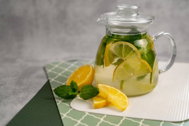 Yeşil desenli bir yüzey üzerinde cam çaydanlıkta limon naneli içecek ferahlatıcı. Yaz içkileri konsepti. Katalog, yayınlar, dergiler için yemek fotoğrafı.