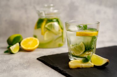 Limonlu sağlıklı buzlu çay ve meyveli bulanık gri arka planda turunçgil dilimli nane. Soğuk yaz limonatasını tazeliyorum.