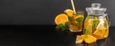 Cam çaydanlık ve koyu arkaplanda narenciye dilimleri olan bir bardak soğuk portakal suyu. Doğal ferahlatıcı içecek. Metin için yeri olan pankart. Restoranlar ve kafeler için yaz içeceği kavramı.