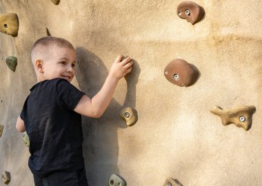 Yazın bir spor sahasında yapay kaya duvarına tırmanan küçük bir çocuğun portresi. Çocuk sporu ve sağlıklı yaşam tarzı. Okulda beden eğitimi.
