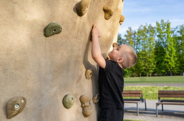 Küçük çocuk yazın spor sahasında yapay kaya duvarına tırmanıyor. Okulda beden eğitimi. Çocuk sporu ve sağlıklı yaşam tarzı.