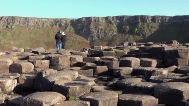 Kuzey İrlanda, İngiltere 'deki Bushmills' in Giants Causeway 'inde birbirine kenetlenmiş 40.000 bazalt sütunun keyfini çıkaran insanlar.