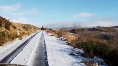 Driving through the snow covered Glenveagh National Park in the shadow of a mountain - County Donegal. Republic of Ireland.