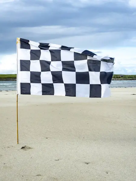 Black and white flag waving on the sandy beach.