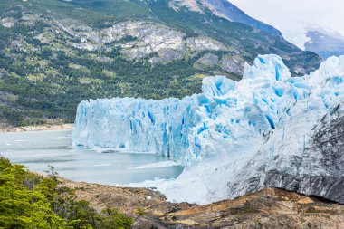 Perito Moreno buzulunun güçlü turkuaz buzu ve sağda küçük bir turistik gemi. Los Glaciares Ulusal Parkı, Arjantin