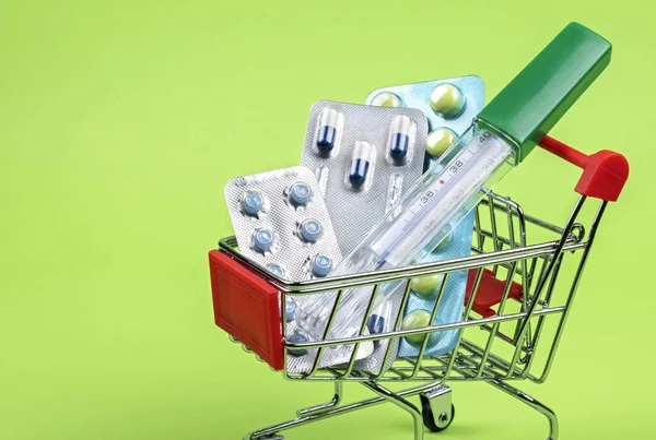 Thermometer, pills, tablets and vitamins in a shopping cart on green background. Concept: shopping and delivery of medicines