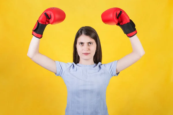 自信的年轻女子 戴着红色拳击手套庆祝胜利 举起双手弯曲手臂肌肉 在黄色背景下被孤立的坚强而坚定的女孩的画像 自卫概念 — 图库照片