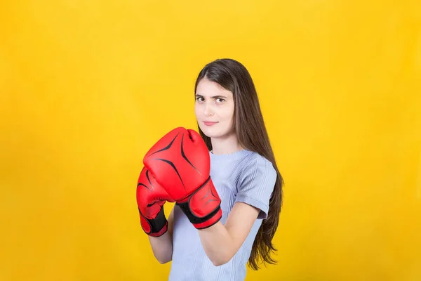 自信的年轻女子戴着红色拳击手套站在战斗的位置上 一个坚强而坚定的女孩的画像 准备在黄色背景下被隔离的战斗 自卫概念 — 图库照片
