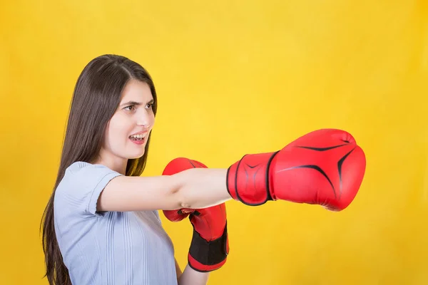 怒气冲冲的年轻女子戴着红色拳击手套站在战斗的姿势上 用手打了一拳 一个坚强而坚定的女孩的画像 准备在黄色背景下被隔离的战斗 自卫概念 — 图库照片