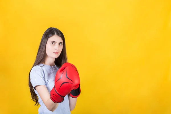 自信的年轻女子戴着红色拳击手套站在战斗的姿态上 一个决心坚定的女孩的画像 在黄色背景下与复制空间隔离 准备战斗 自卫和领导概念 — 图库照片