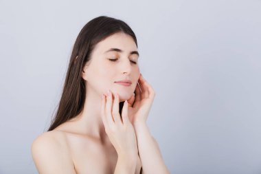 Genç ve güzel bir kadın yüzüne dokunuyor ve yepyeni bir krem kullandıktan sonra ipeksi dokunuşların tadını çıkarıyor. Sağlıklı vücut ve akıl kavramı.